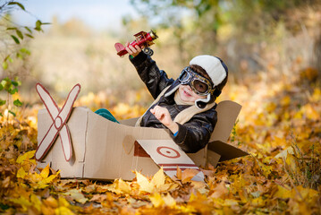 A happy child dreams of traveling in an airplane and plays an airplane pilot. The kid sits in a cardboard plane and pretends to be a pilot in the park in the fall. © sergo321