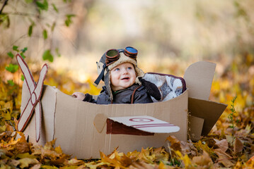 A happy child dreams of traveling in an airplane and plays an airplane pilot. The kid sits in a cardboard plane and pretends to be a pilot in the park in the fall. © sergo321