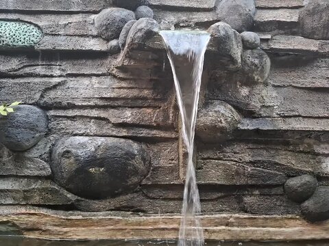 Water flowing down artificial stone waterfall fountain in garden pond, steady shot