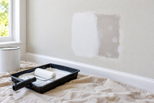 Drywall patch half covered with white primer beside small roller in paint tray - priming stage of drywall repair