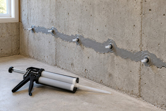 Epoxy paste over wall crack with injection ports and dual cartridge gun on floor - foundation crack repair