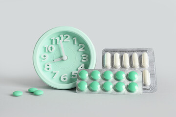 Fototapeta premium Medication adherence and healthcare schedule, clock with pill blisters and tablets for daily treatment routine and medical management on grey background