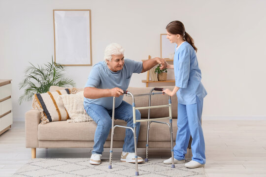 Elderly care and assisted living, nurse helping senior man stand up from sofa with walker for mobility support and physical rehabilitation in home