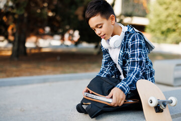Schoolboy putting books into backpack beside skateboard © djile
