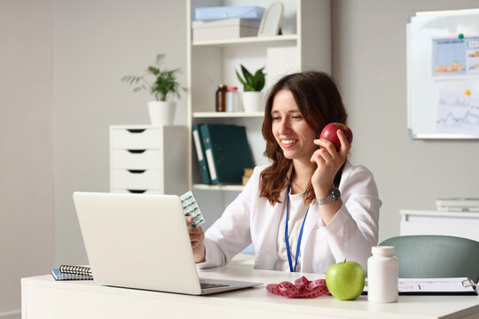 Telemedicine and nutrition counseling, nutritionist holding apple and pills during video call on laptop in medical office for healthy lifestyle advice