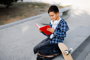 Schoolboy reading red book outdoors with skateboard © djile