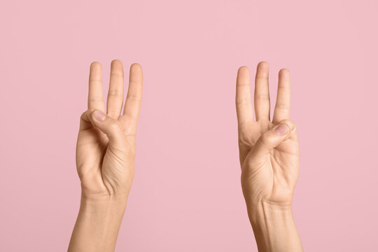Communication and counting concept, hands showing number three with fingers raised in gesture on a solid pastel pink background for visual messaging