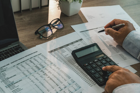 Businessman using calculator and pen to review financial reports, supporting tax preparation, accounting document checking, financial statements and business calculations.