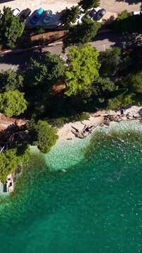 Croatia, aerial view of the coastline with clear turquoise sea, beach, cars parked along the road, and lush green trees