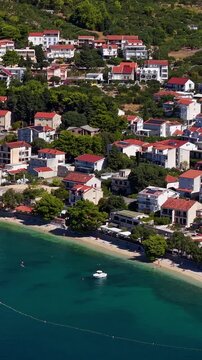 Croatia, aerial view of coastal village with red tile roofs, green hills, and turquoise sea