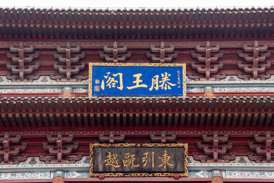 Close-up of ornate traditional Chinese architectural details featuring the 'Tengwang Pavilion' blue plaque and 'Dongyin Yue' inscription on red-painted wooden eaves with intricate dougong brackets