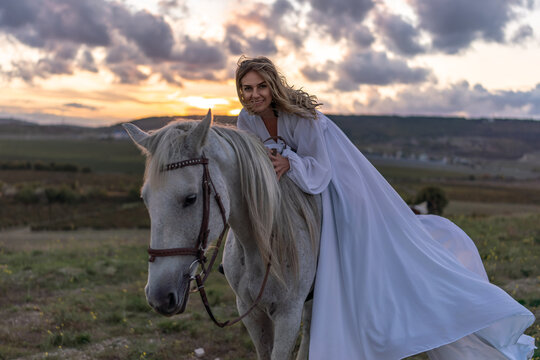 Woman horse sunset, elegant young blonde female rider on a white steed in the wild field