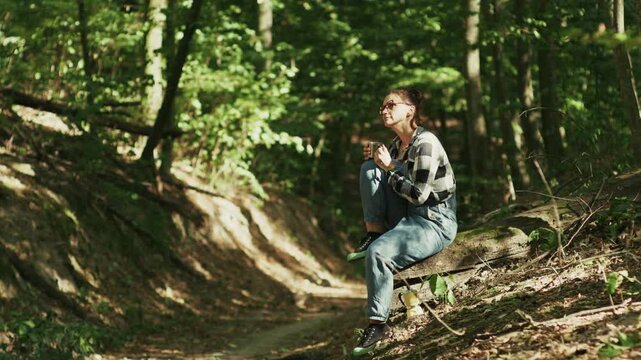 Woman Drinking Coffee while Sitting on Log in Sunlit Forest