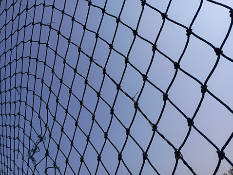 Broken black rope net against clear blue sky