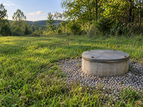 Sealed wellhead with steel cap in a grassy rural clearing