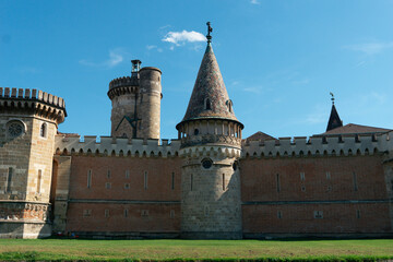 medieval castle fortress wall towers battlements red brick and stone blue sky, franzensburg castle in laxenburg park near vienna austria with conical spire and green lawn, sunny summer day © Lana Pietukhova