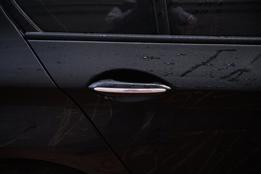 Close-up of a black car door handle with chrome silver trim, wet from rain with water drops on the surface.