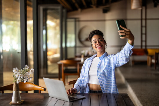 Successful digital nomad woman working on laptop and taking a selfie in a tropical resort office