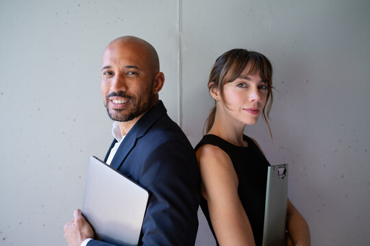 Business team standing back to back with laptop and clipboard indoors