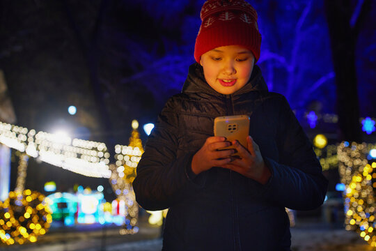 Smiling girl using smartphone outdoors at night with Christmas lights
