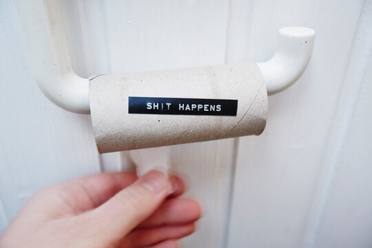 Hand reaching for an empty toilet paper roll with message shit happens