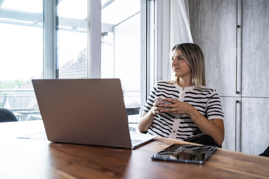 Young woman relaxing with coffee at her home office desk