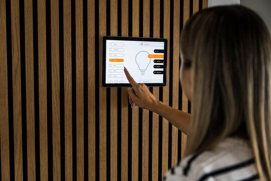 Woman controls smart home lighting on a wall mounted tablet
