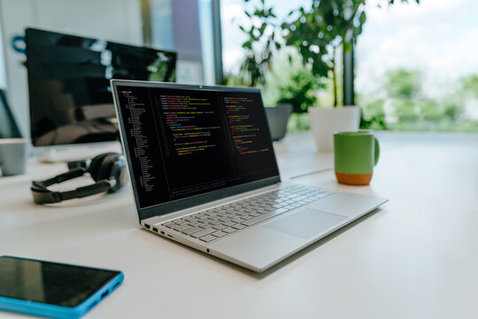 A modern laptop displays programming code on an office desk