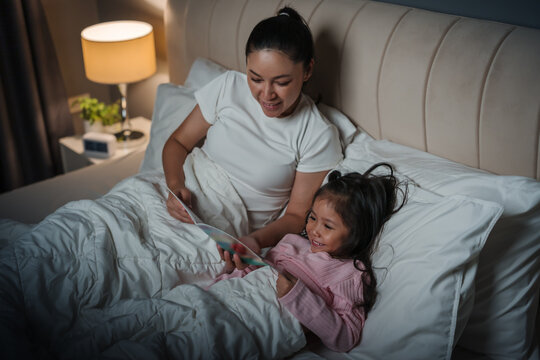 happy mother read story in the book for preschool child girl in bed at night