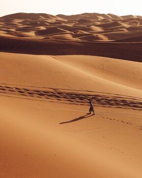 Merzouga, Draa-Tafilalet, Morocco - 08 July 2026: View of a person walking across the rolling sand dunes in the Sahara Desert, casting a long shadow on the golden sand.