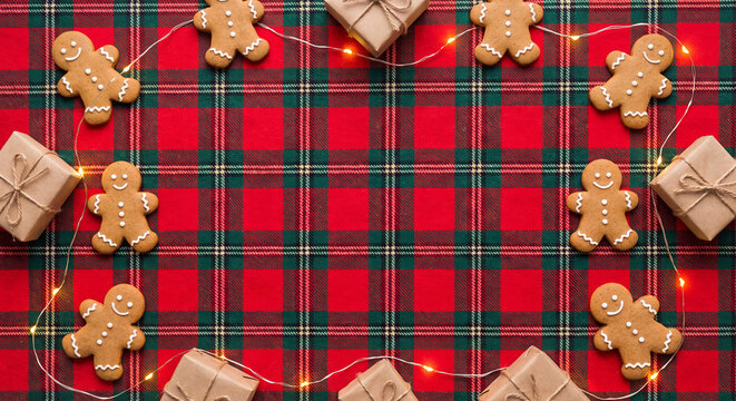 Gingerbread cookies and fairy lights on a red tartan plaid fabric for festive Christmas background