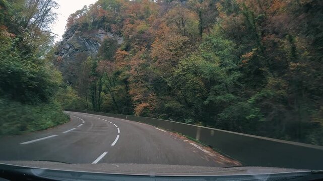 Route de montagne sinueuse traversant une for&ecirc;t aux couleurs automnales, envelopp&eacute;e de brume sous un ciel couvert. Une atmosph&egrave;re calme et myst&eacute;rieuse au c&oelig;ur d&rsquo;un paysage naturel de montagne.