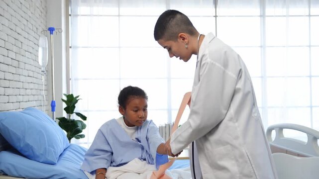 Caucasian female doctor wounding bandage around of little African American girl arm in hospital room