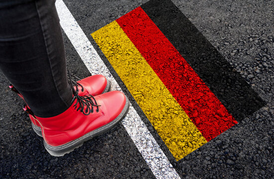 a woman with a boots standing on asphalt next to flag of  Germany and border
