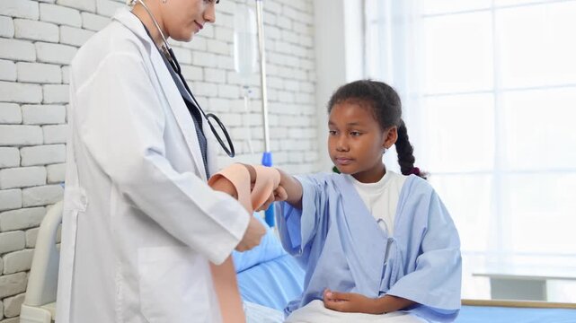 Caucasian female doctor wounding bandage around of little African American girl arm in hospital room
