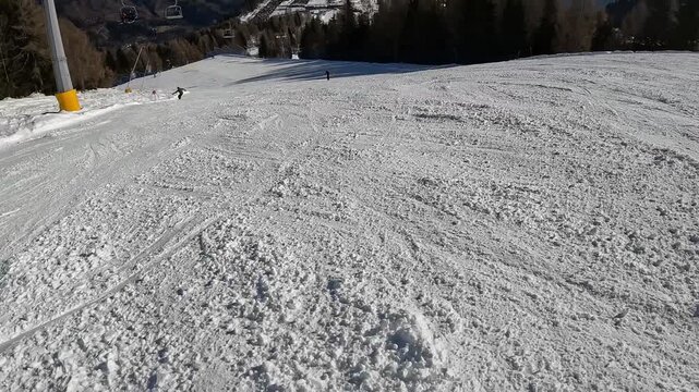 POV skiing downhill passing a yellow Rallentare slow down warning sign on the piste. Winter sports safety in an Italian alpine ski resort.