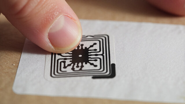 Composition showing a gloved finger or part of a hand making direct contact with a small RFID tag on a label affixed to a package