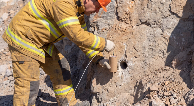 Worker inserting explosive wire into drilled rock hole at an open quarry mining site
