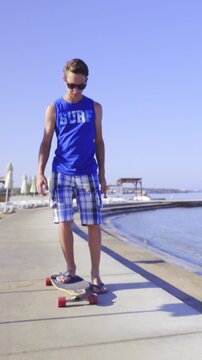 Surf boy riding longboard at sea wearing sunglasses