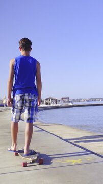 Teenager in blue shirt riding longboard on concrete beach