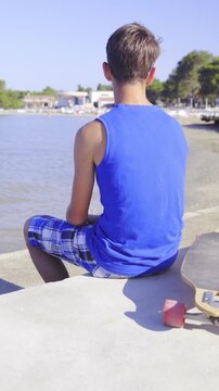Teenager with longboard sit on beach with view on sea