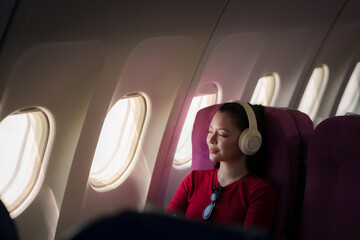 Asian female traveler relaxing with headphones inside an airplane cabin, enjoying a peaceful journey while flying to her vacation destination. © Witoon