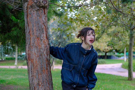 Young woman standing beside large tree trunk in autumn park looking up thoughtfully, contemplation, nostalgia, daydreaming, solitude, peaceful walk, nature connection and relaxation concept, copy spac