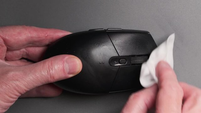 A person wipes a computer mouse with a damp cloth to remove dust and residue.