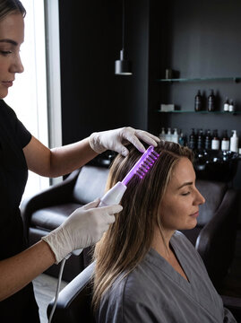 Cosmetologist performing high frequency comb scalp therapy on client in salon