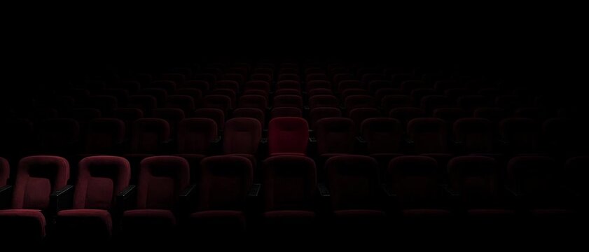 Empty cinema hall with rows of red velvet seats in dark spotlight