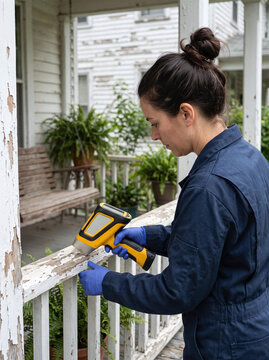 Female inspector using an XRF analyzer to test old porch railing for lead paint