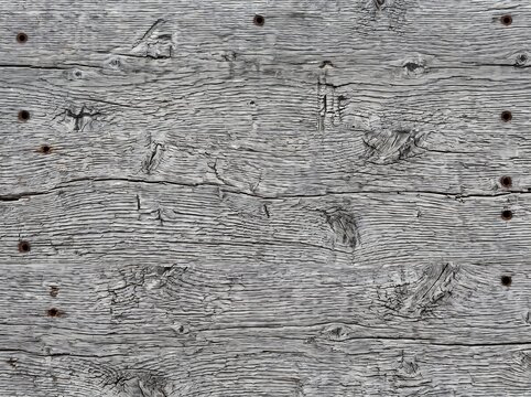 Macro close-up photograph of weathered gray barn wood texture featuring rough planks, deep grain lines, natural knots, and rusted nail holes