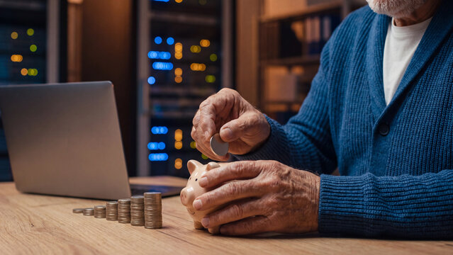 Retirement savings and pension planning concept, senior man putting coin into piggy bank with rising coin stack and laptop for future money saving and financial security