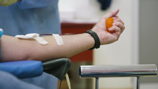 Bright indoor clinic light illuminating a patient squeezing an orange ball during donation.